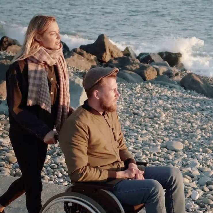 A woman and a man in a wheelchair strolling by the ocean