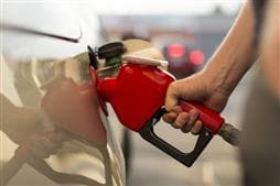Hand holding a fuel nozzle at a gas pump and filling their car