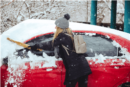 Woman brushing snow off a car