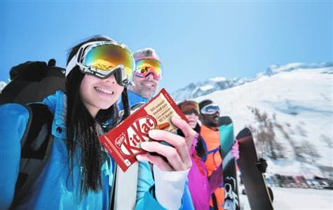 A group of skiiers and a woman holding a KitKat chocolate bar.