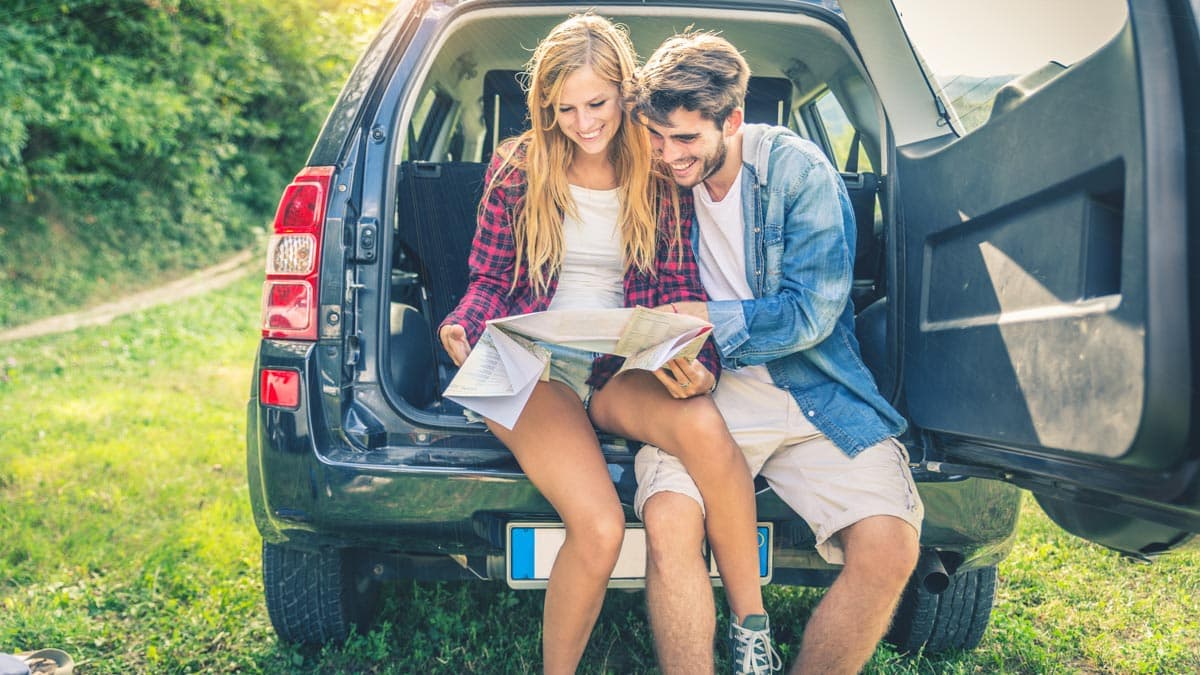 A man and a woman sitting in the back of their SUV and reading a map