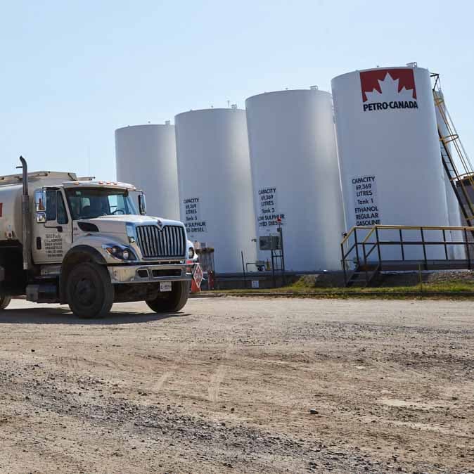 A Petro-Canada truck next to some large fuel tanks