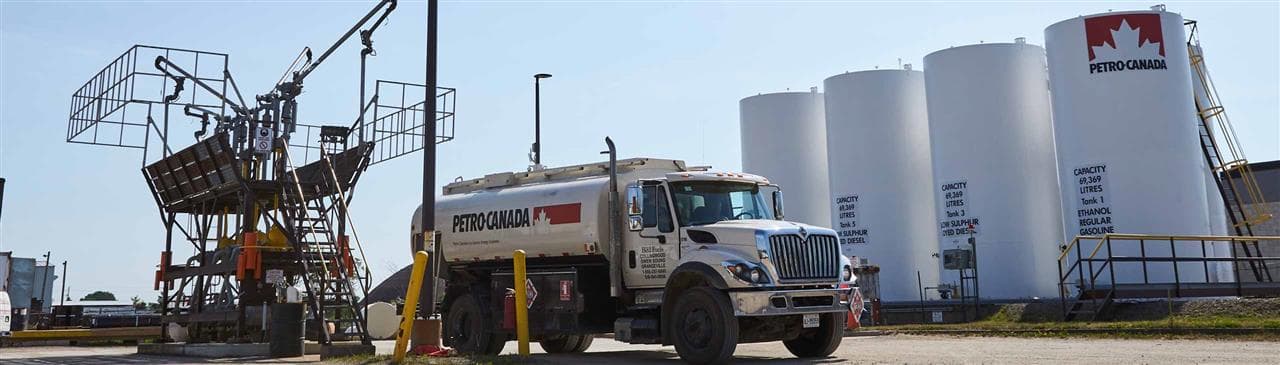 Un camion Petro-Canada devant une rangée de gros réservoirs de carburant.